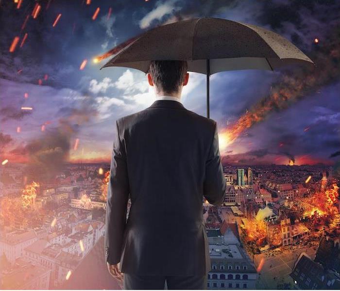 man holding an umbrella looking at a city burning